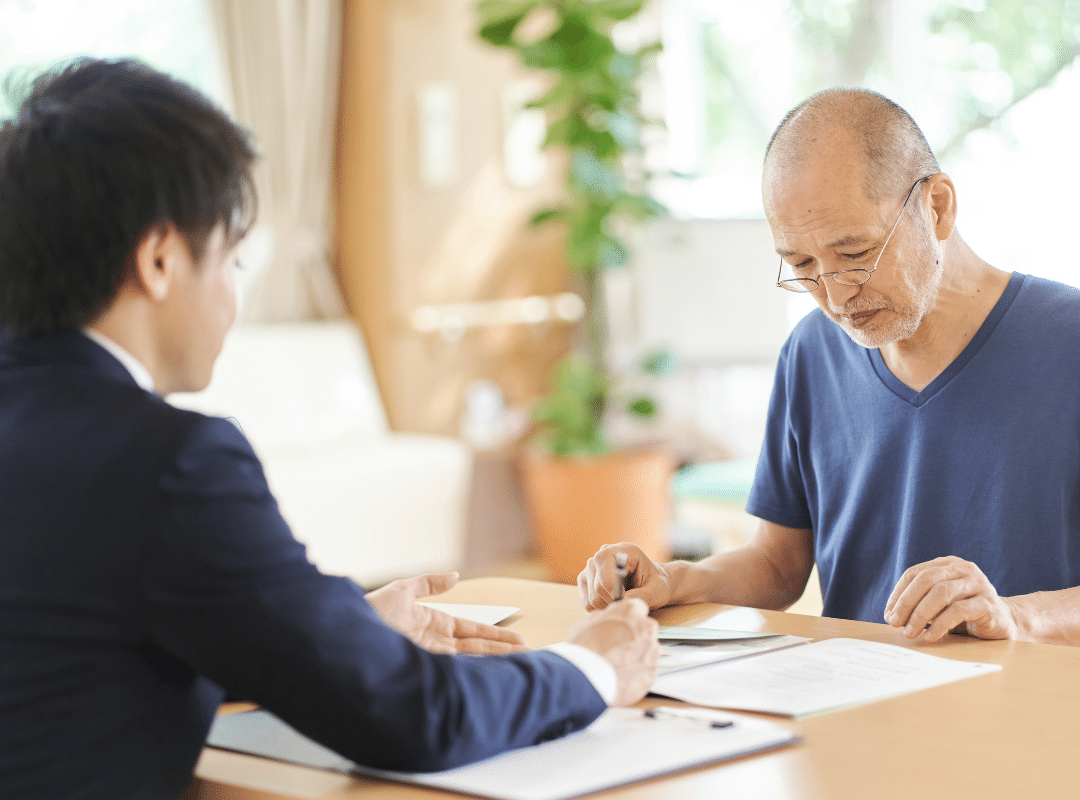 An older man seated at a table, writing with a pen on a piece of paper, deep in thought.