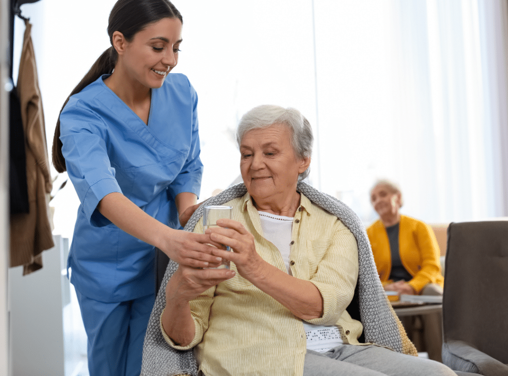 A nurse in uniform offers a cup to an elderly woman, showcasing care and compassion in a healthcare setting.