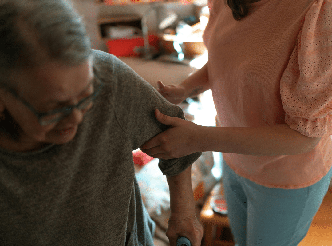 Caregiver assisting senior woman with mobility in a comfortable home setting, illustrating support in daily living for assisted living options.